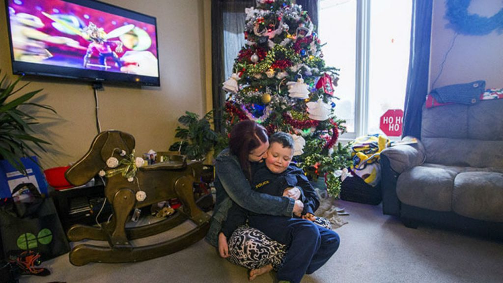 A mom and son sit in front of a Christmas tree in their living room.