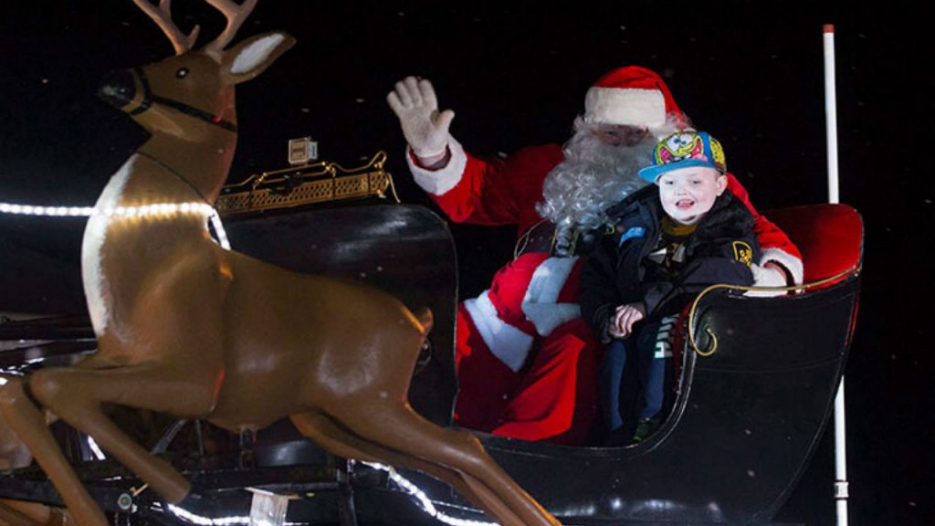 Santa and a young boy sit in his sleigh during a parade.