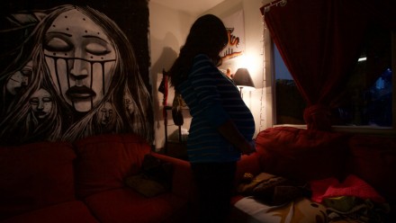 First Nations and the foster care system. Pregnant woman cradling her bump in a dark room