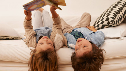 Two kids sitting upside down on the couch reading