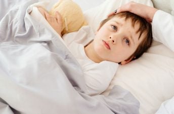 Sick boy in bed with mom's hand on his forehead