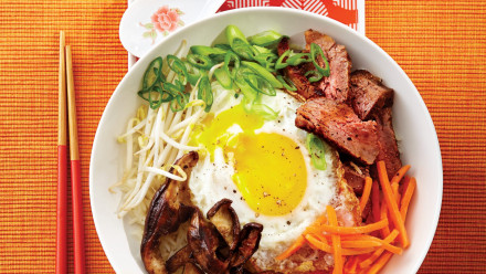 Bowl of rice topped with bean sprouts, beef, mushrooms, carrots, green onion and an egg