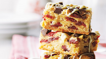 Stack of squares with chopped dried cranberries, chocolate and white chocolate drizzle