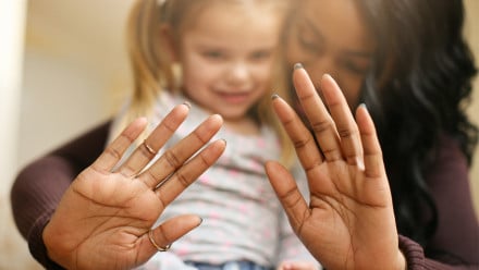 A woman holds up her hands to the camera while holding a small child