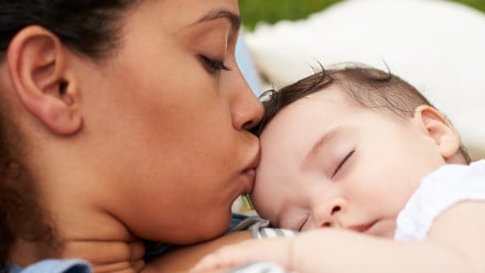 A woman holds and kisses her sleeping baby