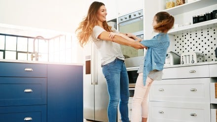 a happy mother and her daughter playfully dancing together at home