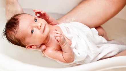 Newborn baby having his first bath in a small tub