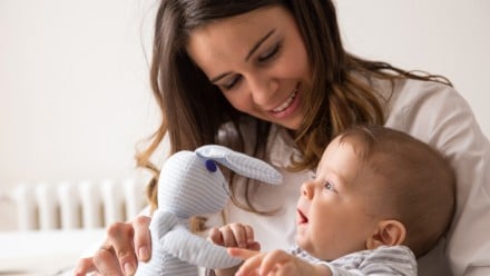 Woman holding her baby and putting a stuffed rabbit to his face