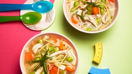 Two bowls of chicken noodle soup with edamame and carrots