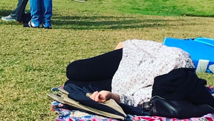 Mom sleeping on the ground at her kids soccer game