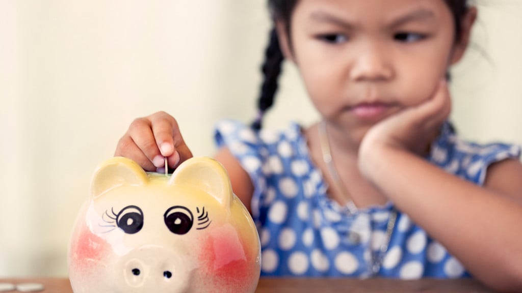 Little girl begrudgingly puts money into her piggy bank