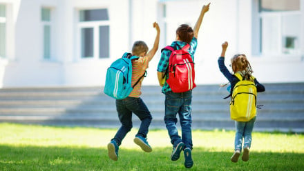 Photo of three kids with backpacks jumping in the air