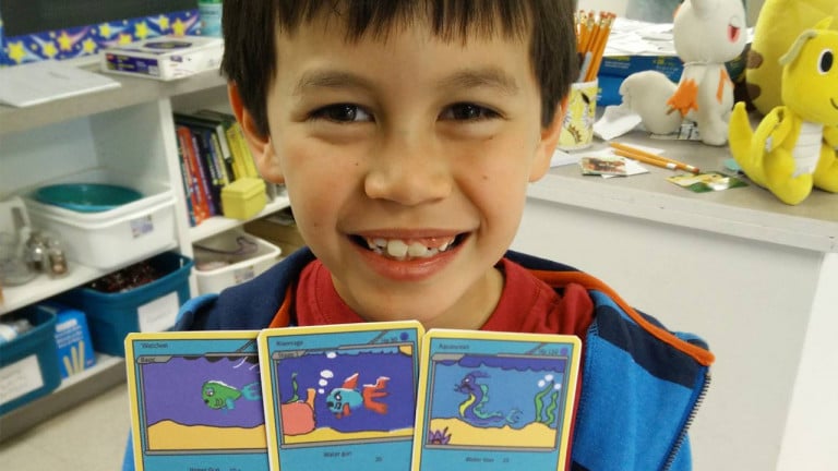 A young boy holds up Pokémon cards he made