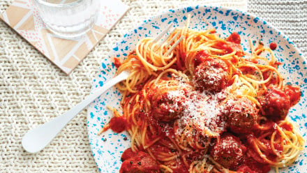 Speckled plate with spaghetti and meatballs topped with grated Parmesan cheese with a fork. Looks very appetizing
