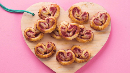 AHeart shaped cookies on a wooden board on a pink background