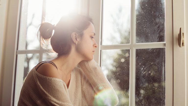 A sad woman sits by a window