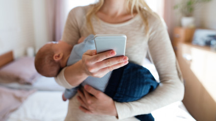 Young mother holding her sleeping baby son in her arms white on her phone
