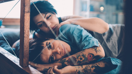 Two women lie in bed together, one tries to comfort the other