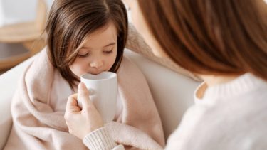 Mom giving hot drink to sick daughter