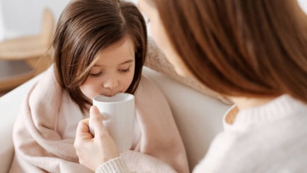 Mom giving hot drink to sick daughter
