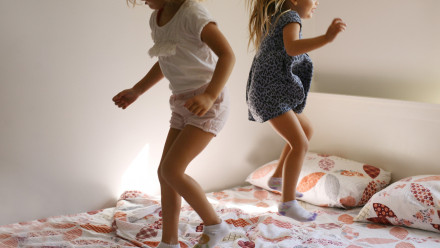 Two little girls jumping on a bed