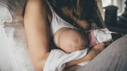 A woman in a nursing bra breastfeeding her baby in bed
