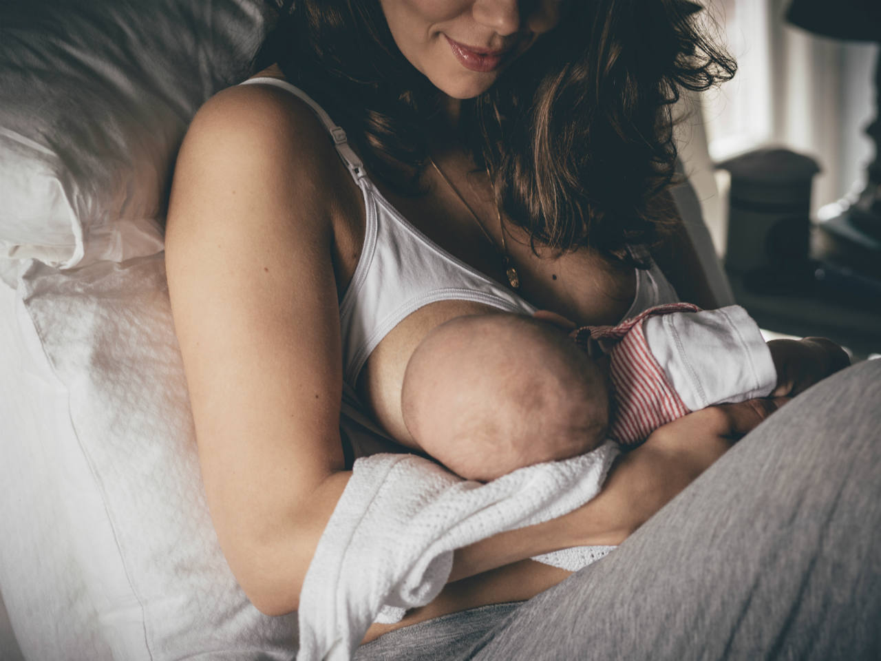 A woman in a nursing bra breastfeeding her baby in bed