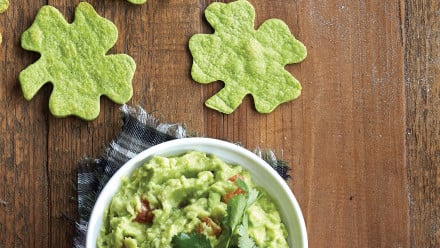 Bowl of chunky guacamole with green clover-shaped tortilla chips