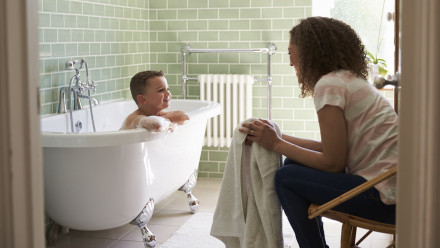 Son in the bath tub for bath time with his mom sitting down with a towel