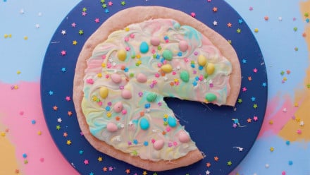 A rainbow pizza with mini eggs and sprinkles on it, on top of a blue plate
