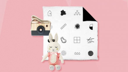 Pink background with minimalist baby toys like a cloth bunny, baby mat and a wooden camera