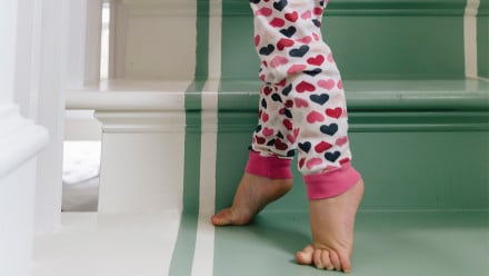 A toddler walks up stairs on her tiptoes