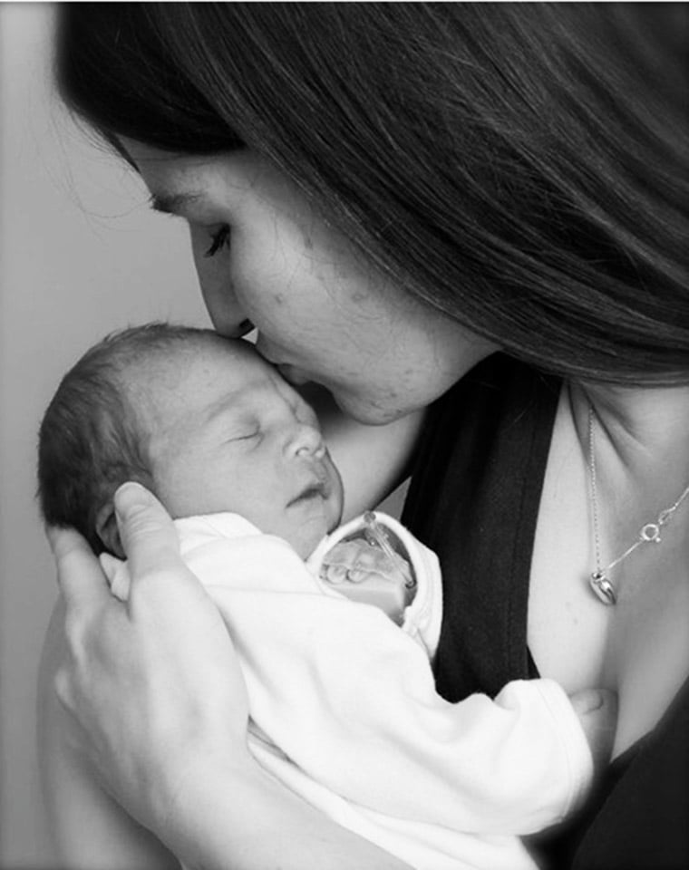 Black and white photo of a mom kissing her newborn baby on top of the head