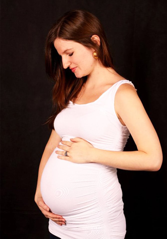 Pregnant woman holding her pregnant belly while looking down smiling