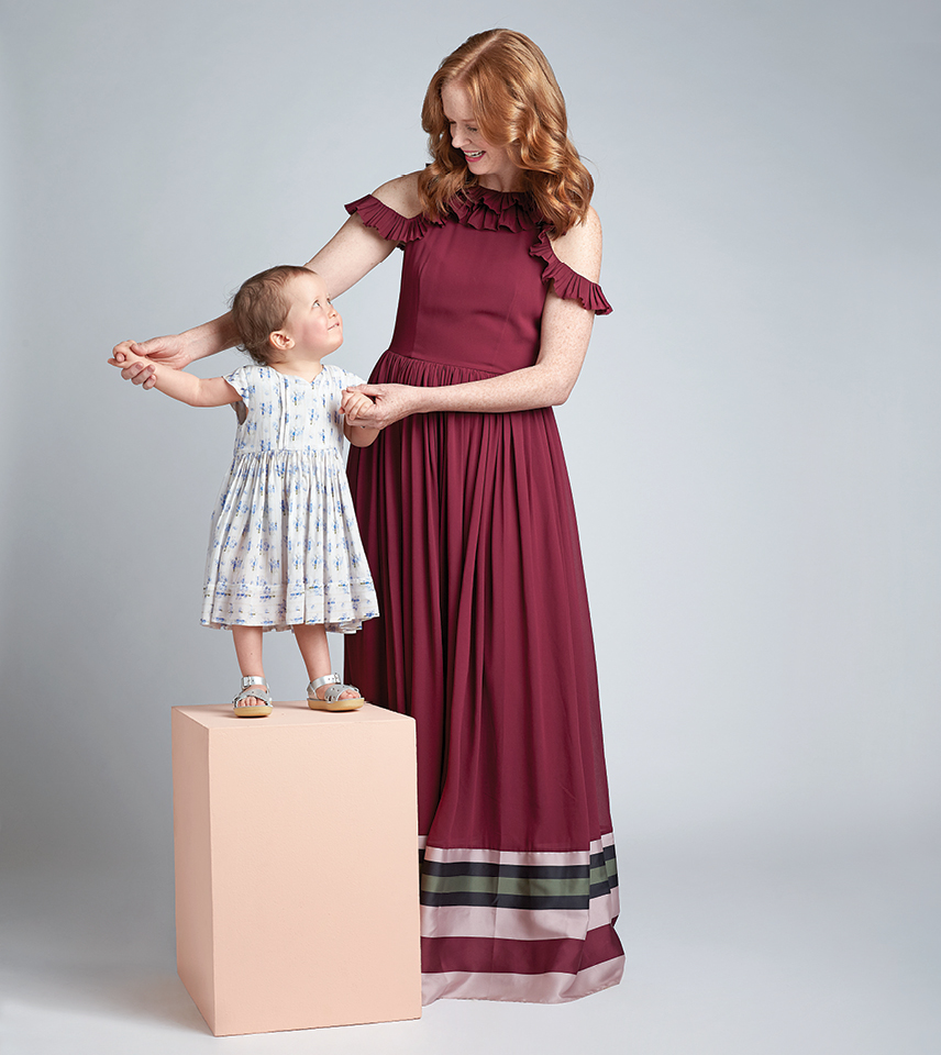 A mom in a dress holds her daughter as she stands on a box