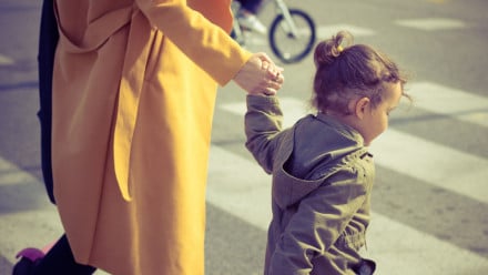 Small girl holding mother's hand while crossing the street at a crosswalk