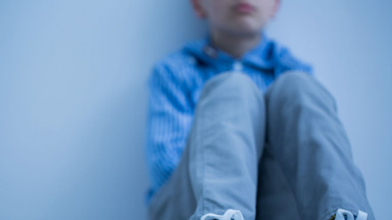 A young boy sitting alone in a corner of a room.