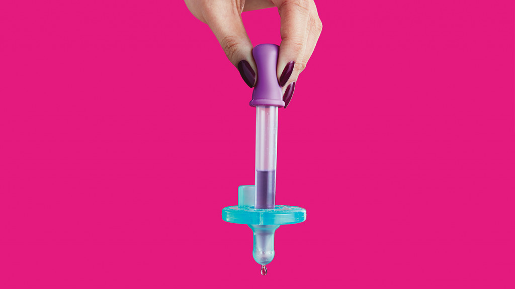 Hand holding a dropper attached to a pacifier in front of a pink background