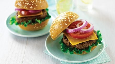 Two burgers on sesame seed buns with cheese, tomato and onion