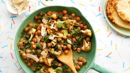 green fry pan with chickpeas, spinach, cauliflower and coconut flakes