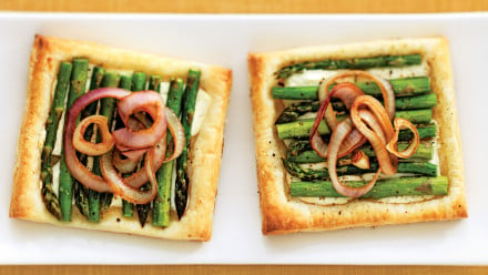 two puff pastry tarts topped with goat cheese, asparagus and red onion