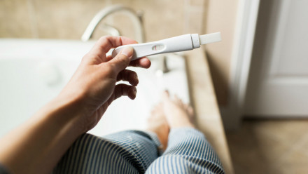 A woman sitting on the edge of a bathtub, looking at a pregnancy test.