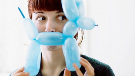 A woman holding a balloon animal to cover her mouth