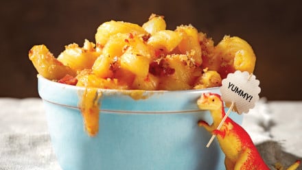 Bowl of cheese spiral pasta with a little dinosaur holding sign that says "yummy"
