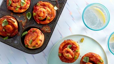 Muffin tin with tiny deep-dish pizzas topped with torn basil