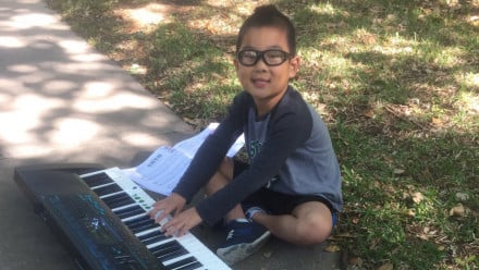 Little boy with glasses sitting on a sidewalk with his keyboard