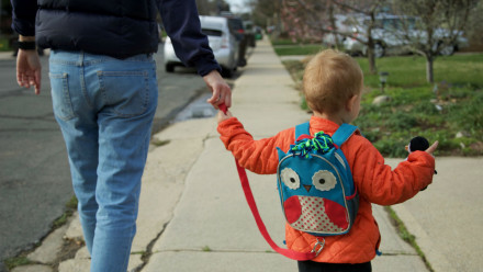 Photo of a kid walking on the sidewalk wearing a leash backpack.