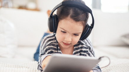 Shot of a young girl wearing headphones while using a digital tablet at home