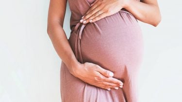 A pregnant woman cradling her belly in a light pink maternity dress