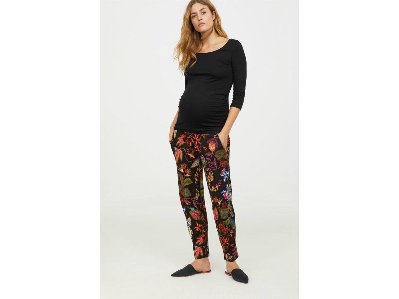 A pregnant woman wearing patterned maternity pants and a black top